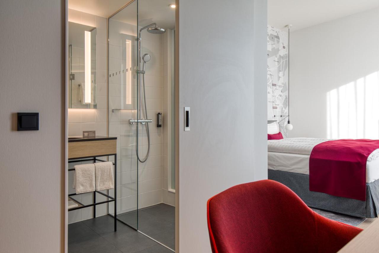 Intercityhotel Berlin Airport Ber Terminal 1 & 2 Schönefeld Exterior foto The photo shows a modern hotel room or bathroom space. On the left, there is a glass-enclosed shower area with a sleek design, featuring a showerhead and minimalist fixtures. Adjacent to the shower, there's a sink area with a stylish countertop and a